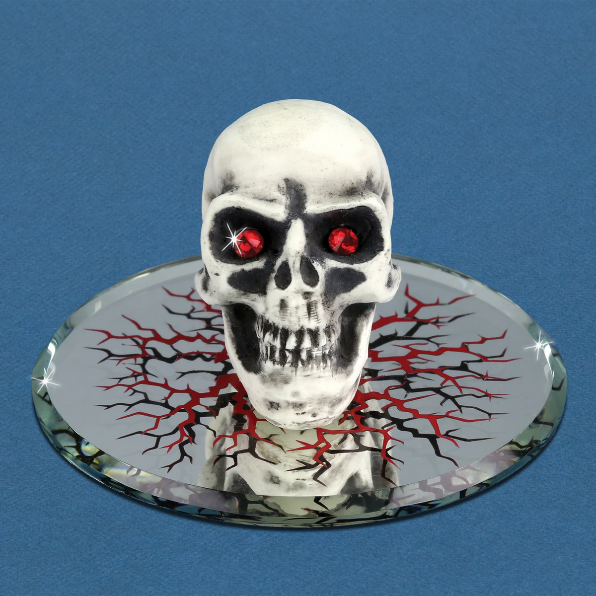 Glass skull figurine with red crystal eyes on a decorated mirrored base