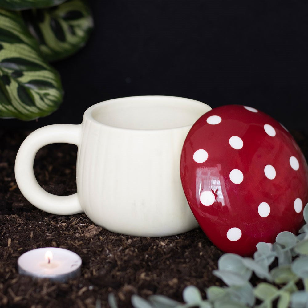 Mushroom mug shown with red and white spotted lid off, nestled in among plants