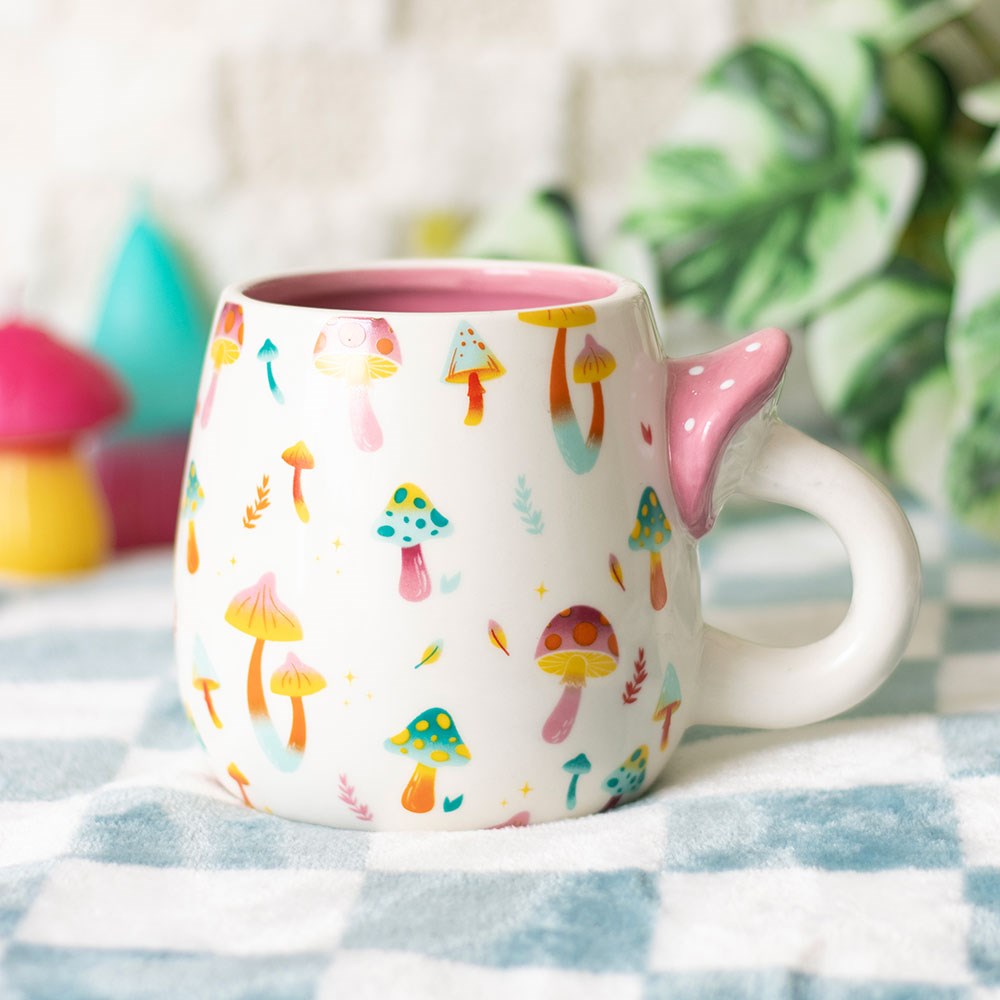 Ceramic mug with colorful mushroom patterns on the outside, handle shaped like a mushroom with a pink top with white spots, pink glaze inside the mug