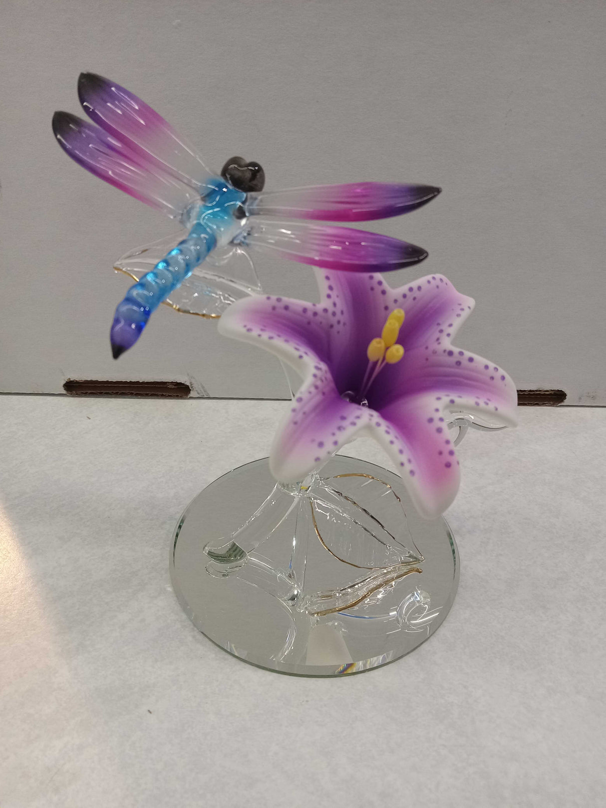 Glass dragonfly perched on a pink and white lily flower with a mirror base