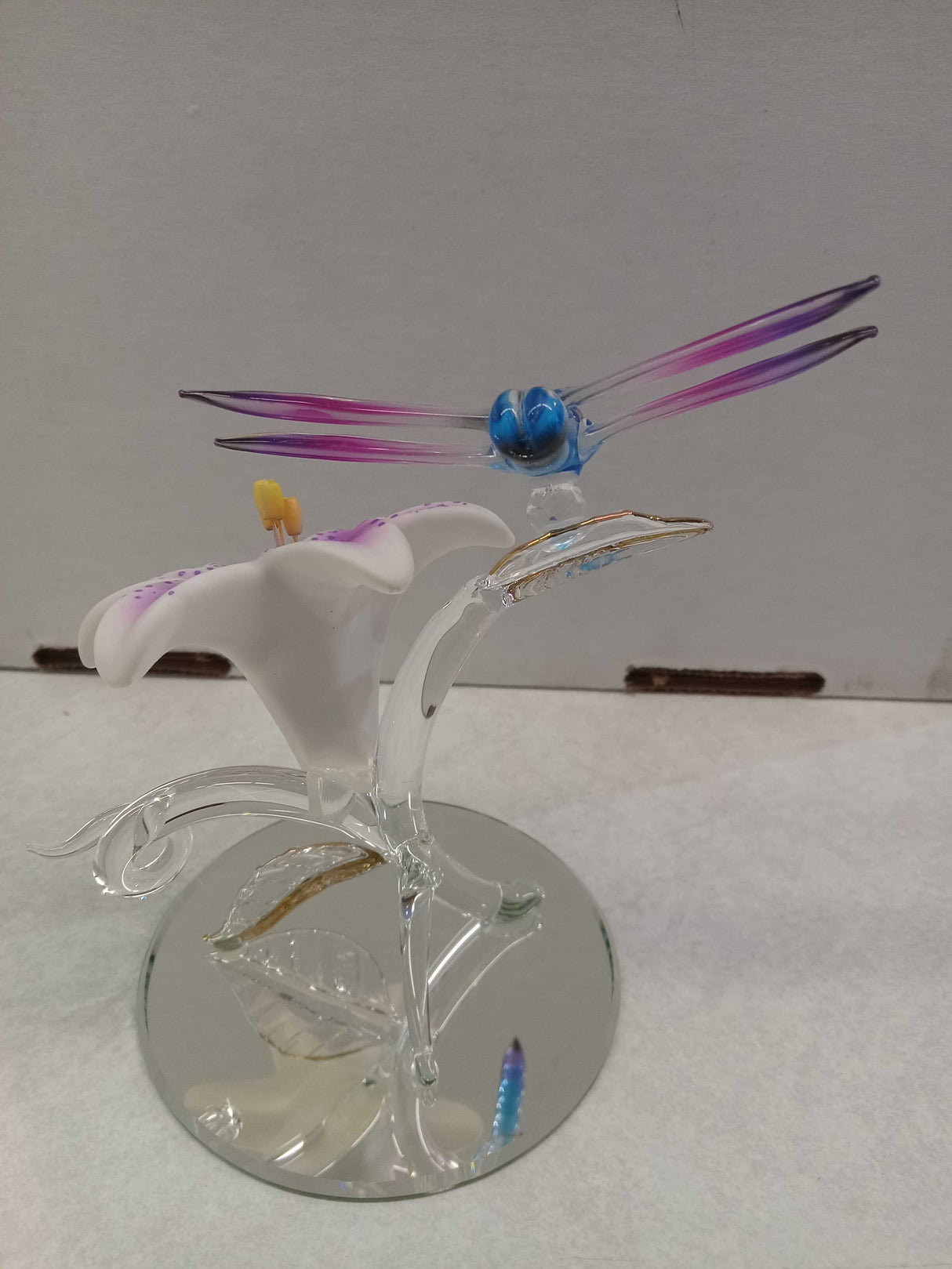 Glass dragonfly perched on a pink and white lily flower with a mirror base, shown from the back