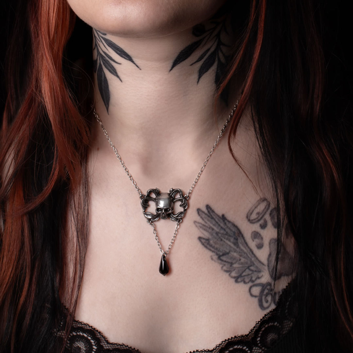 Close-up of a person with tattoos wearing a necklace with a skull pendant.