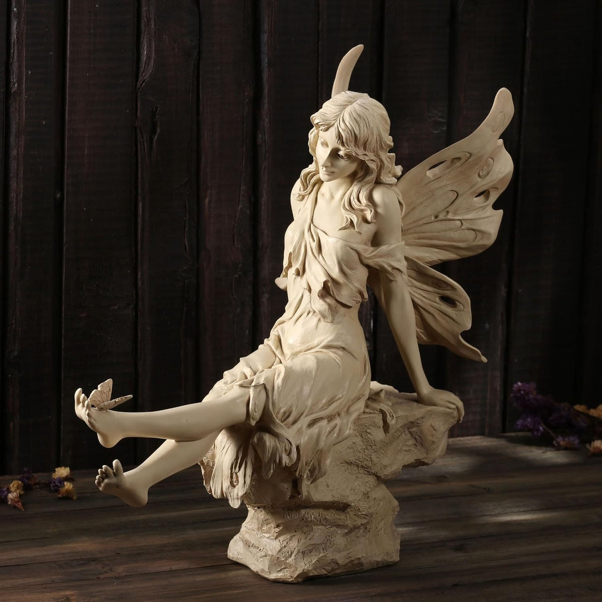 Statue of a fairy with wings sitting on a rock with a butterfly on her foot