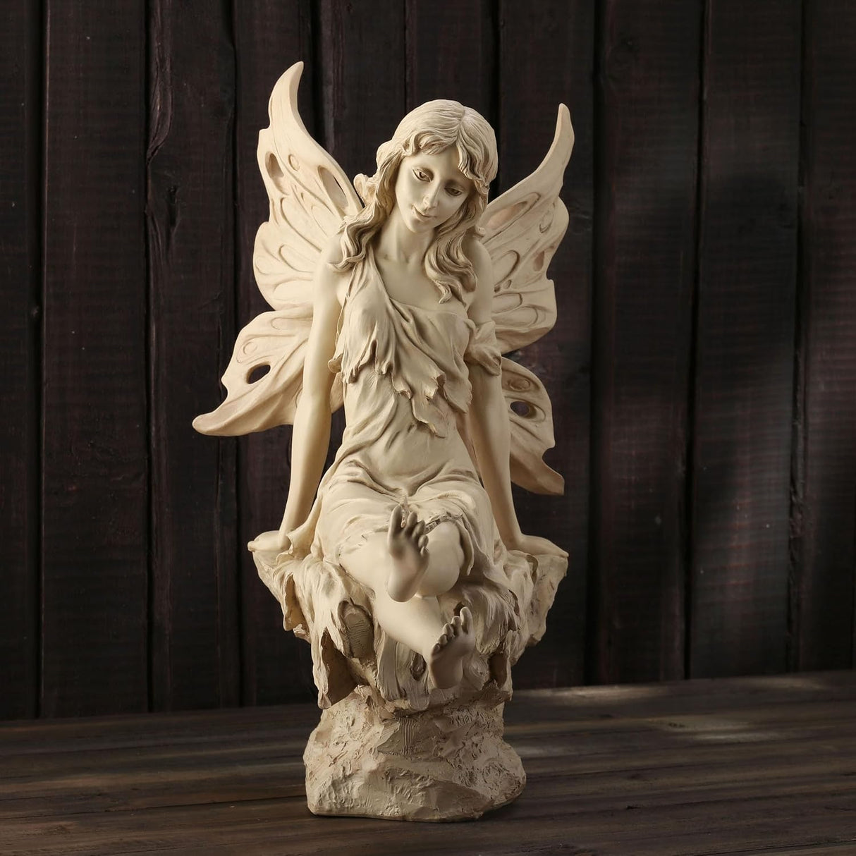 Statue of a fairy with wings sitting on a rock with a butterfly on her foot