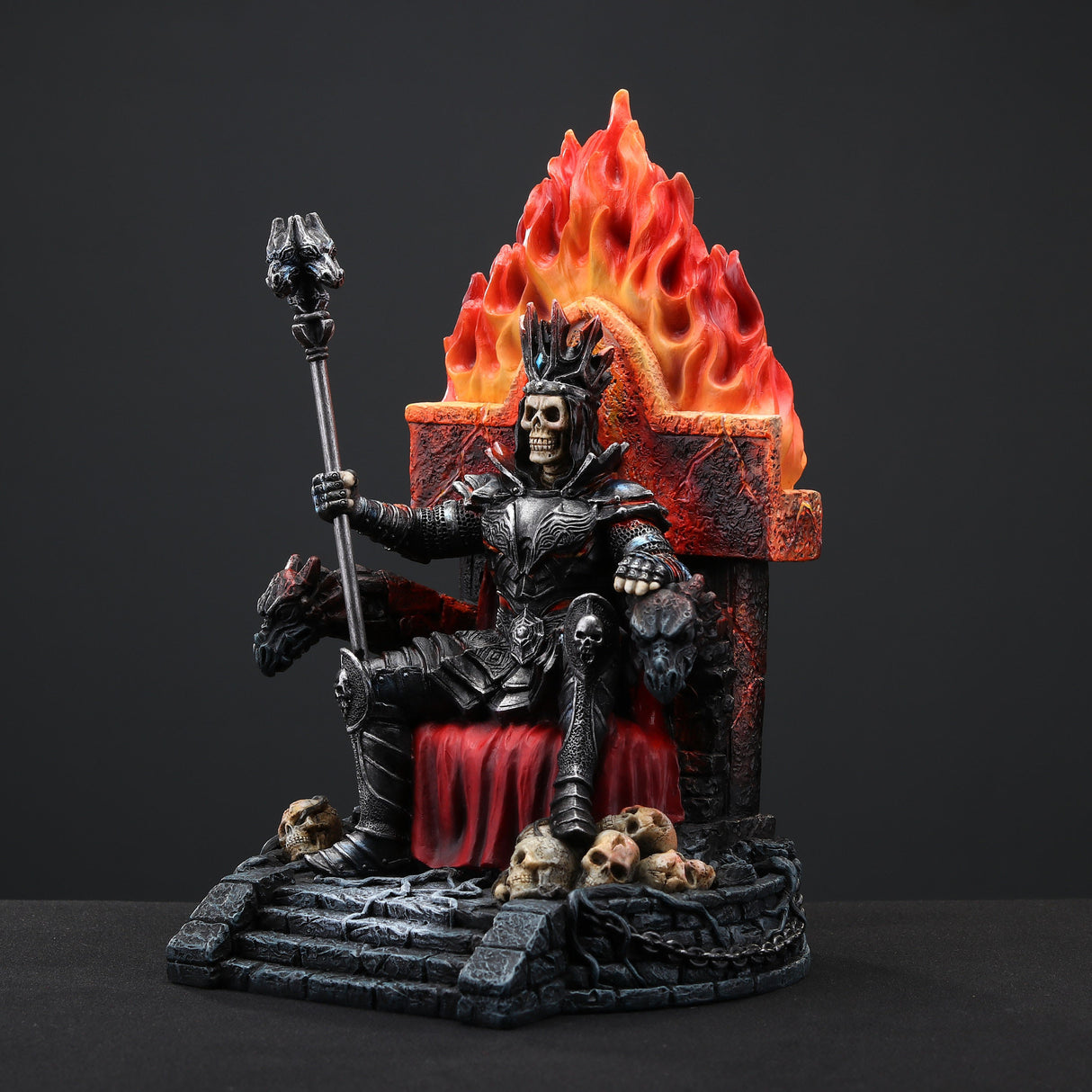 Figurine of skeleton in armor and crown holding staff, sitting on fiery throne with gargoyles, piles of human skulls