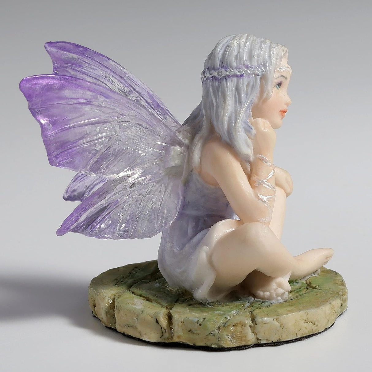 Figurine of fairy with purple-clear wings and pale silver hair sitting cross legged on a mossy stone
