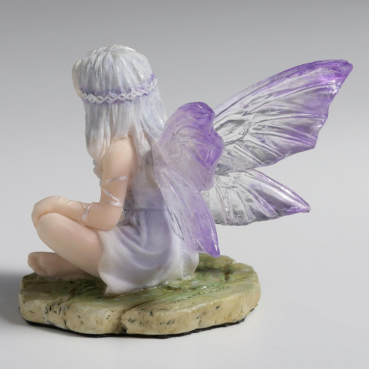 Figurine of fairy with purple-clear wings and pale silver hair sitting cross legged on a mossy stone