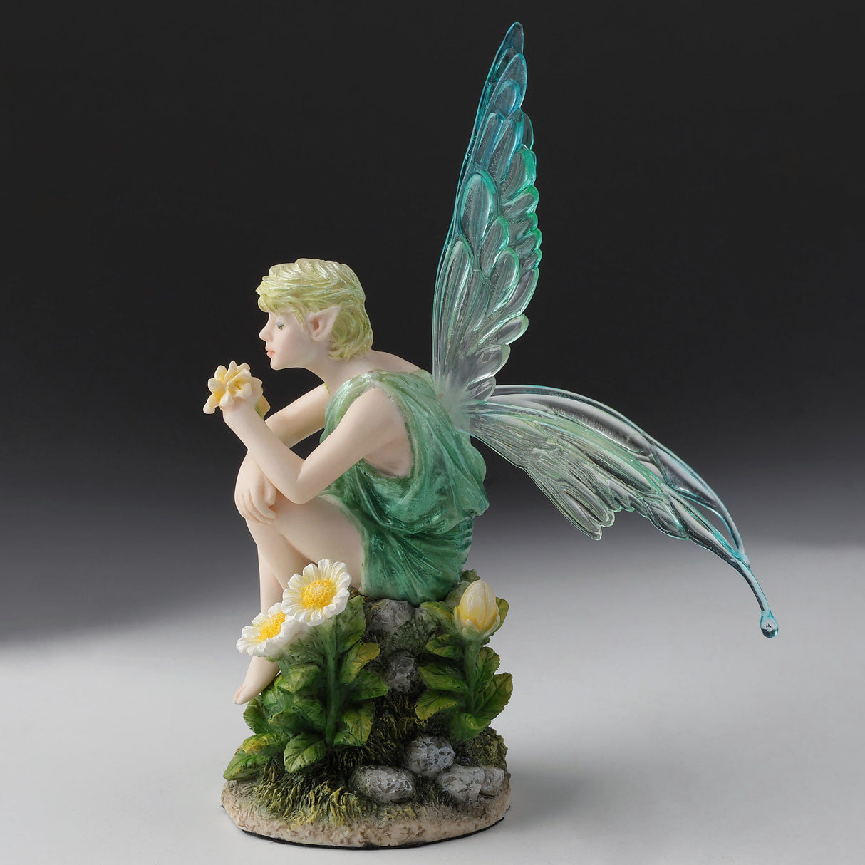 Fairy figurine with green toga and aqua wings sitting on a rock with flowers.