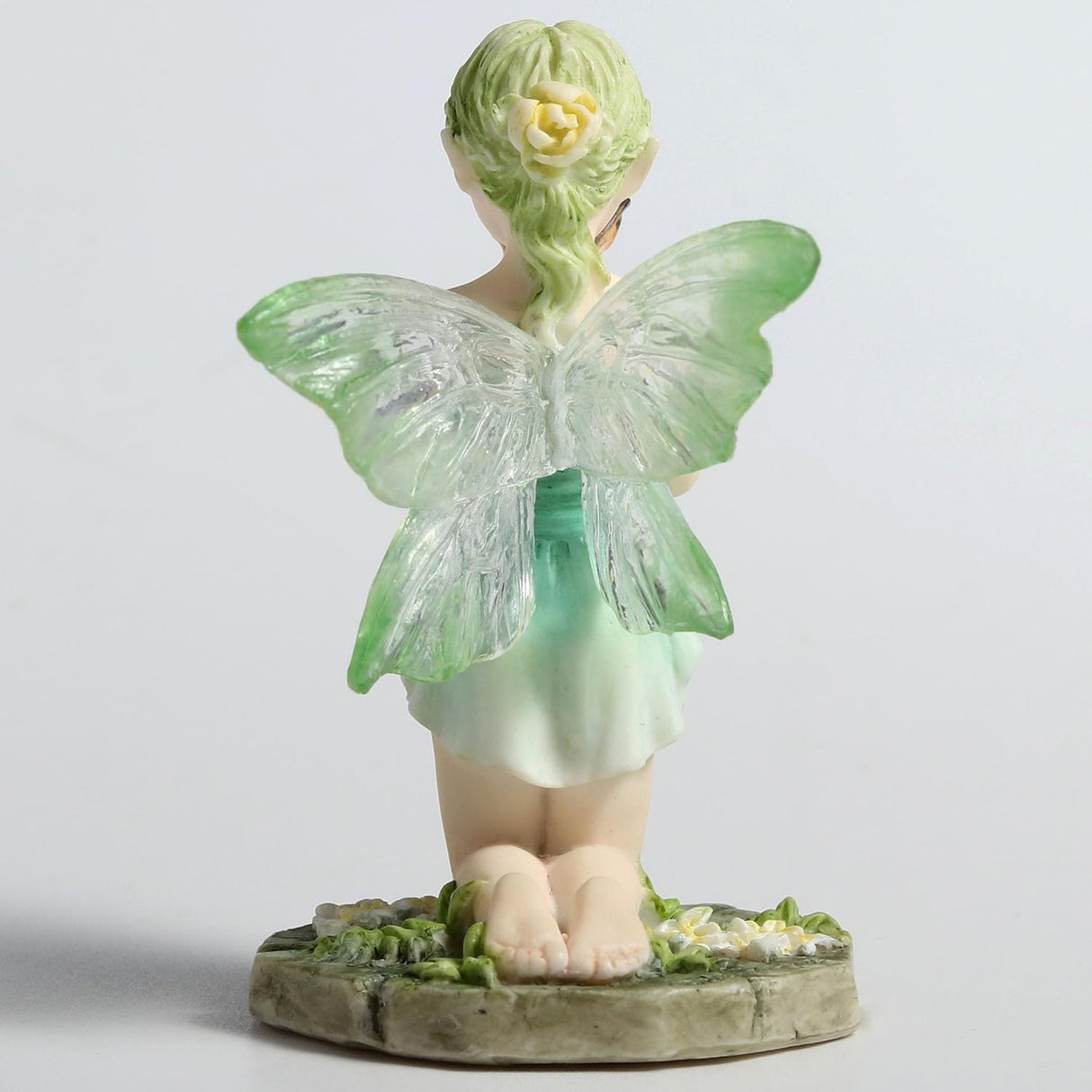 Figurine of fairy in pale green, kneeling with a butterfly, shown from the back, translucent wings