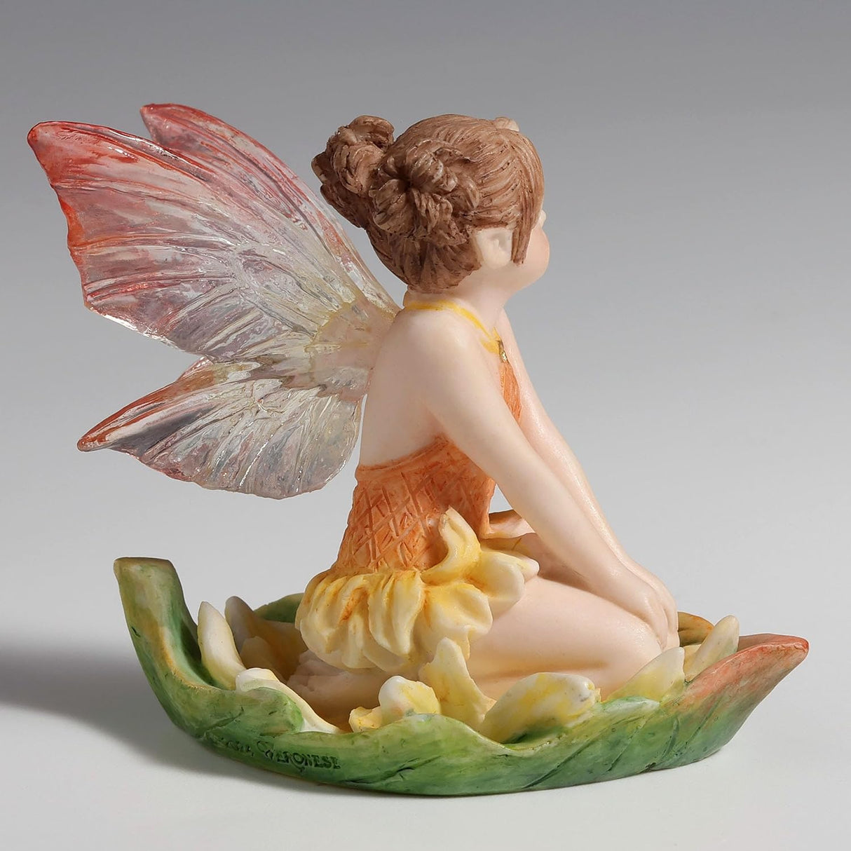 Figurine of fairy in yellow-orange dress with pink and clear wings, reddish-brown hair, blue eyes sitting in a leaf