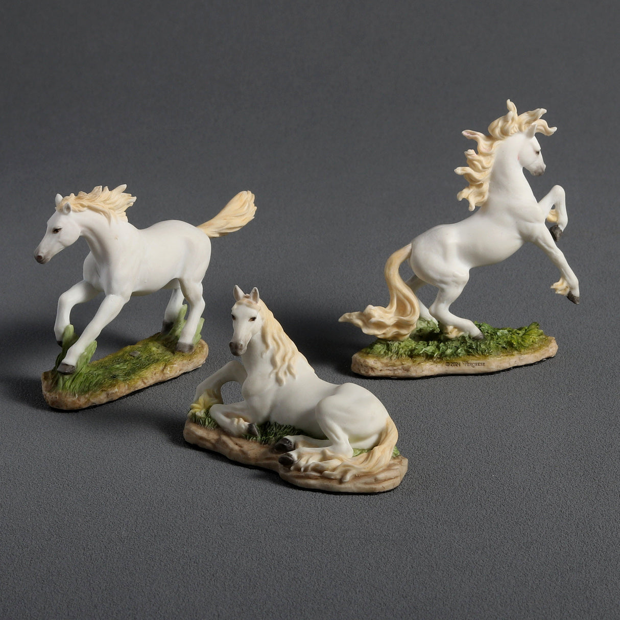 Three white horse figurines on a gray background. Running, prancing, and laying down