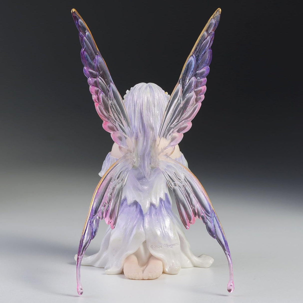 Fairy Figurine, pale purple hair and dress with hands clasped in front of her, eyes closed, transparent wings with shades of purple. Shown from the back