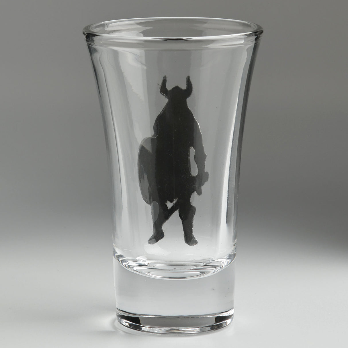 A clear glass shot glass featuring an embossed pewter Viking warrior holding a shield and sword, shown from the back