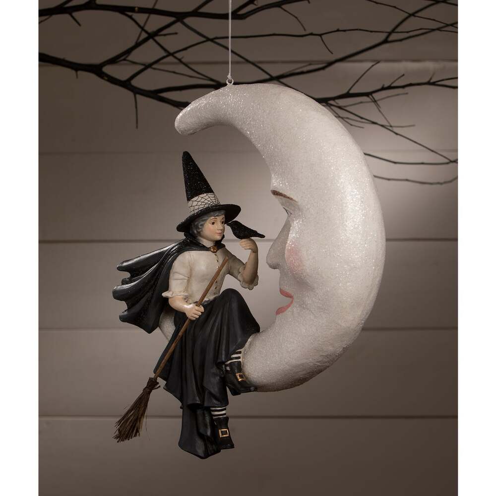 Hanging ornament with a witch on a moon, against a neutral background
