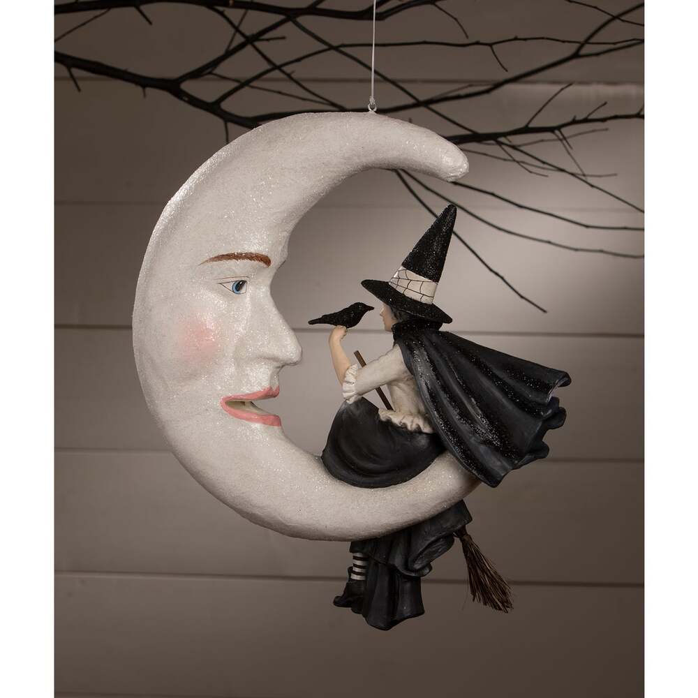Decorative Halloween ornament with a witch on a moon against a neutral background.
