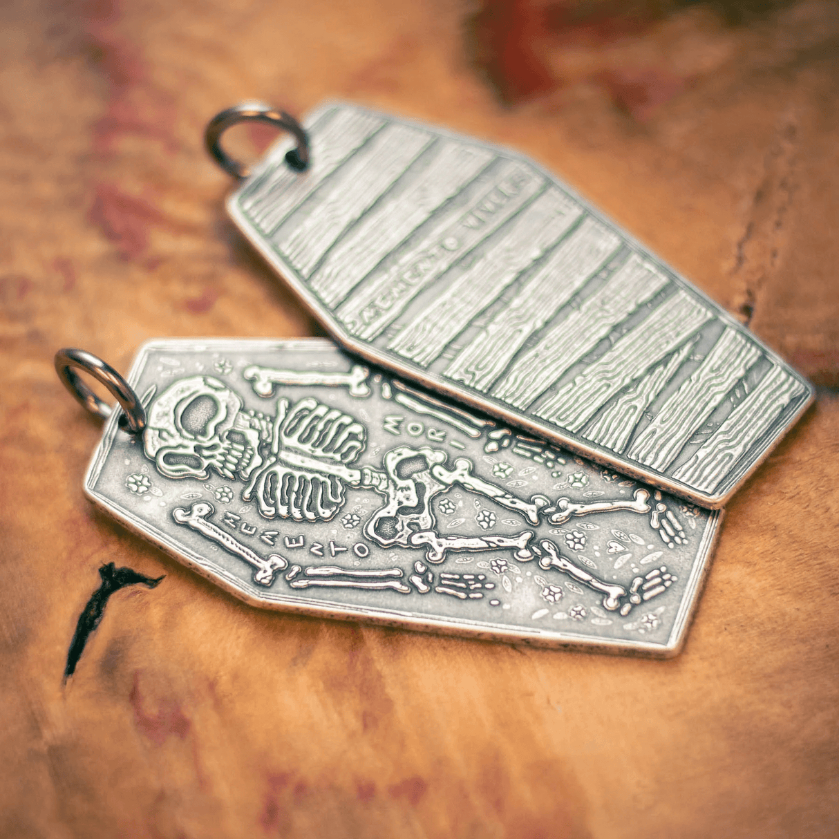 Silver charm featuring a skeleton and the phrase "Memento Mori", backside is wooden coffin with "Memento vivere"