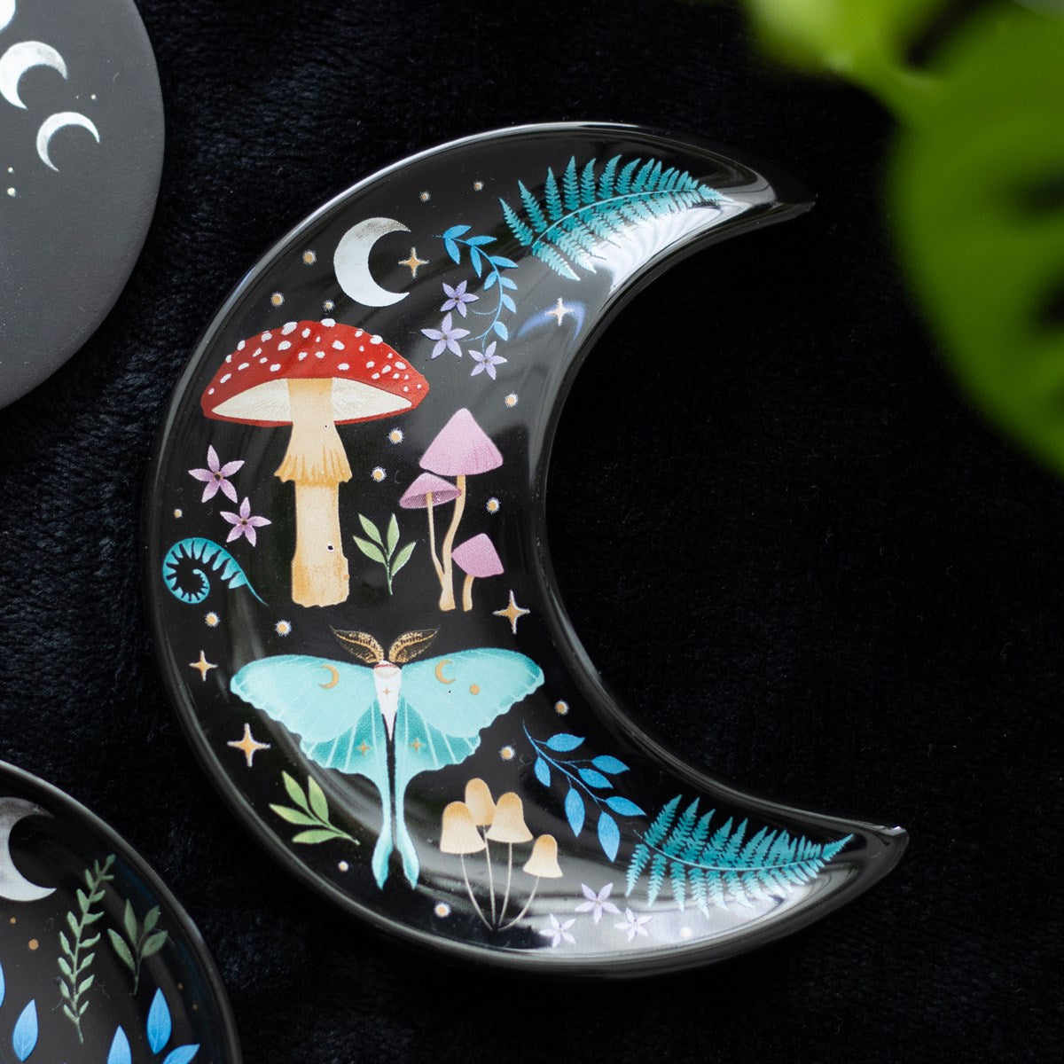 Decorative trinket dish shaped like a crescent moon with mushrooms and luna moth design on a dark background