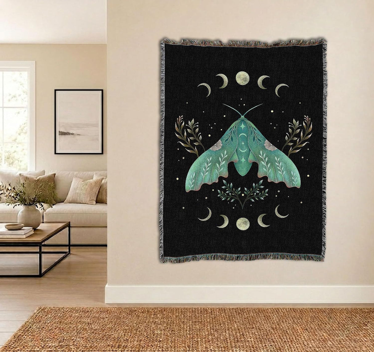A black woven wall tapestry with a large teal moth and moon motifs, hanging on a beige wall in a modern living room setting.