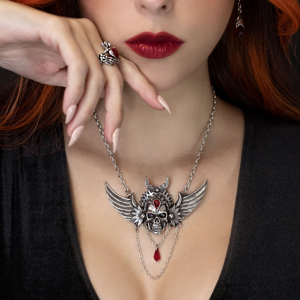 Woman wearing a silver necklace with a skull and wing design, red lips, and red hair.