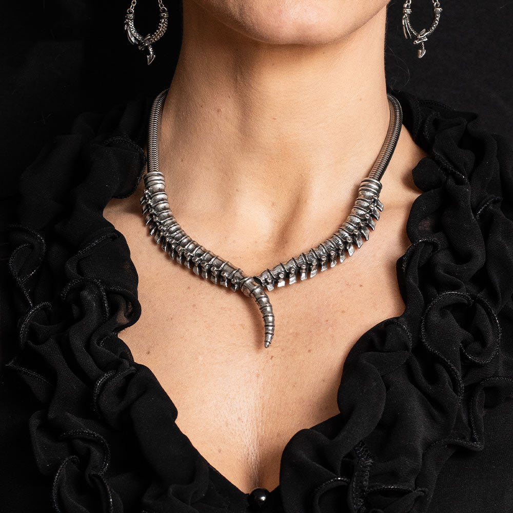 Pewter necklace featuring a human spinal column design, shown worn with dragon earrings