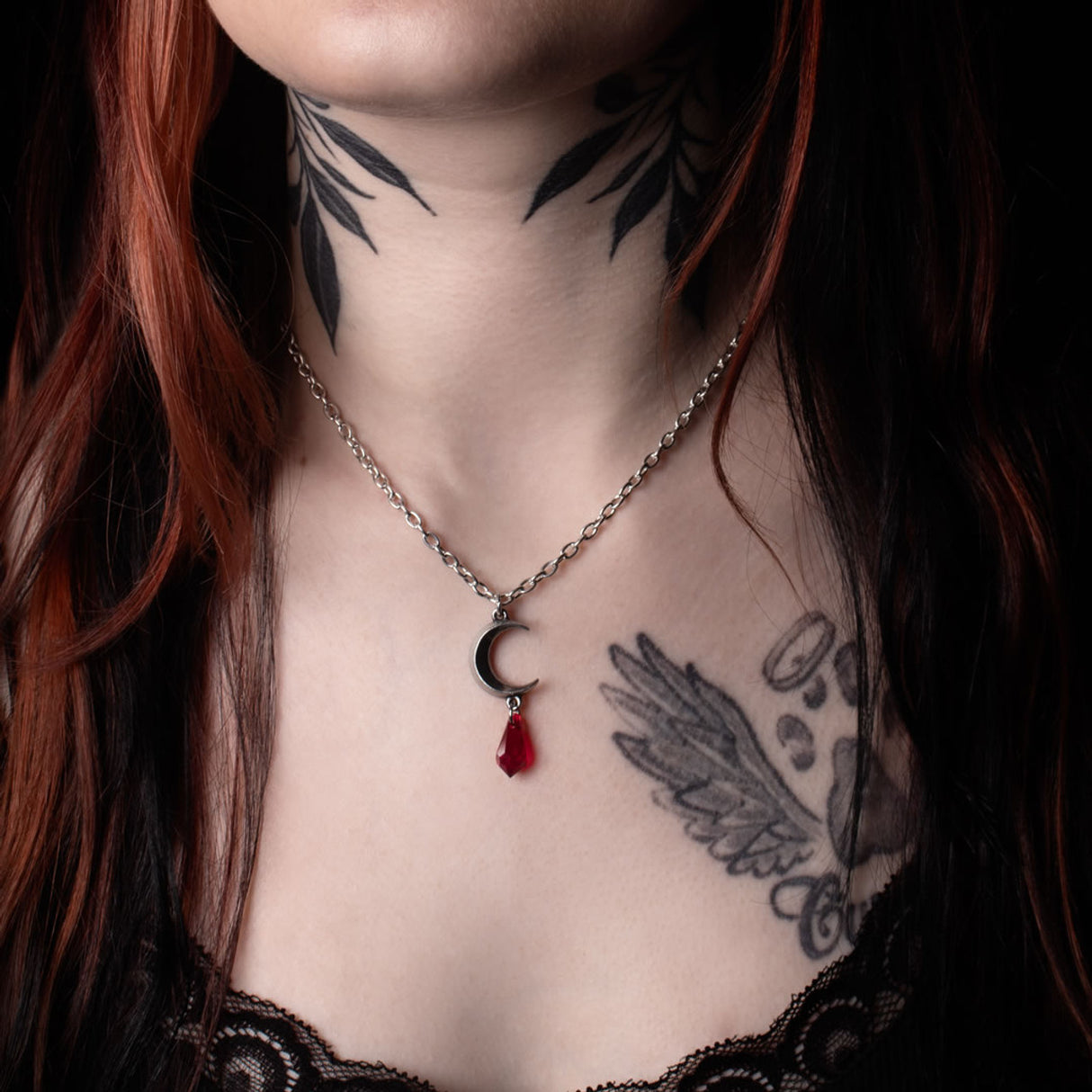 Pendant necklace with pewter crescent moon charm and crystal dropper in red, shown worn
