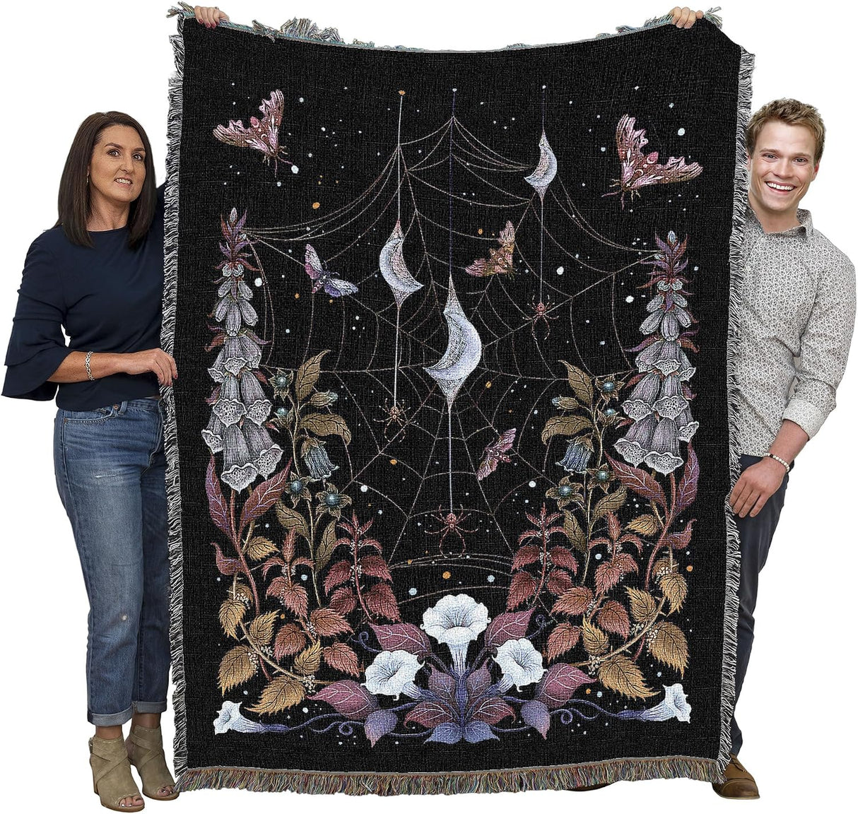 Two people holding a decorative blanket with spider web and moth design against a black background