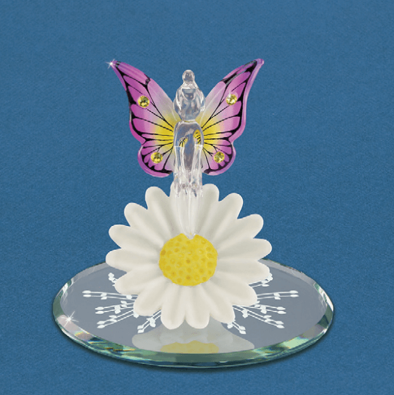 Figurine by Glass Baron. A clear glass fairy with pink and yellow wings sits on a white daisy flower with a yellow center. The pixie has yellow crystal accents on the wings. The base of the piece is a mirror with white designs.