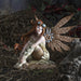 Steampunk fairy figurine with mechanical bronze wings and red hair. Goggles on her head and a striped outfit. She sits on a rock, gazing out. Shown displayed amidst chain netting