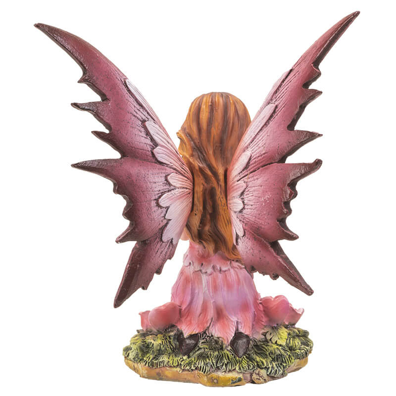 Fairy with pink dress and wings, with hearts on wings. She holds a heart and sits next to rose flowers on the grass. Shown from the back