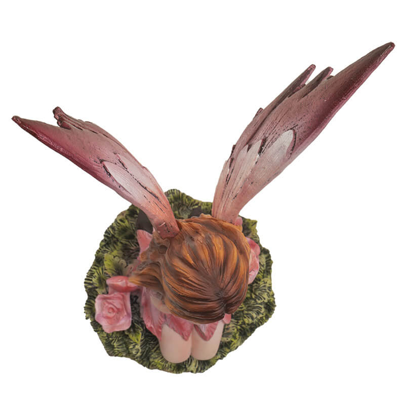 Fairy with pink dress and wings, with hearts on wings. She holds a heart and sits next to rose flowers on the grass. Shown from above, top-down