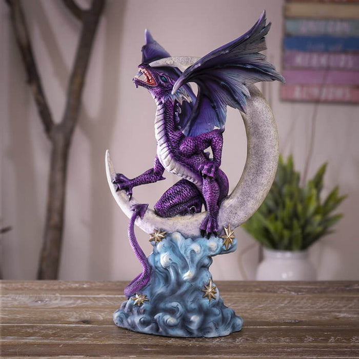 Purple dragon perched on a crescent moon with silver stars and blue clouds. Shown on a wooden table with room background