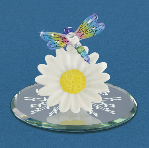 A rainbow winged glass dragonfly with jewel accents perches on a white glass daisy flower with a cheerful yellow center. The Glass Baron figurine has a mirror base with white accent designs.
