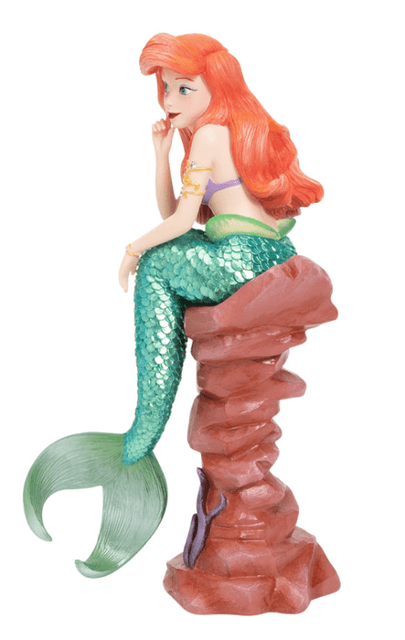Disney's Ariel, the Little Mermaid, sits and ponders. She has a shiny metallic tail and bright red hair.