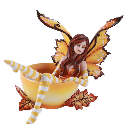 Fairy with auburn hair and orange wings sitting in a cup of tea surrounded by fall leaves. Yellow and white striped sleeves & stockings.