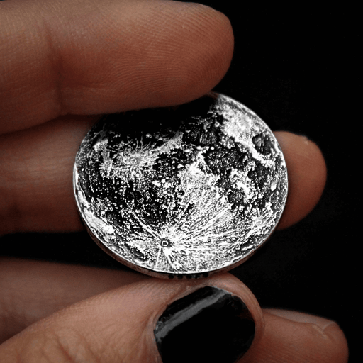 Silver full moon coin shown held in hands with black nail polish