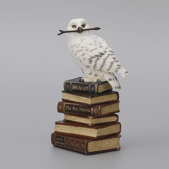 The lovely figurine features a stack of books on magic and witchcraft. Perched on top is a snowy owl, holding a magic wand in its beak. Snowy owl holding wooden wand. Perched on book stack