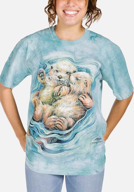 Aqua mottled t-shirt with two otters floating and holding hands, art by Jody Bergsma, shown on an adult