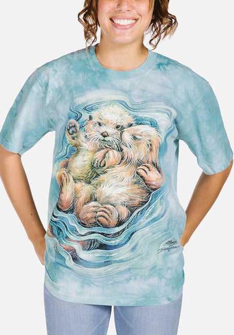 Aqua mottled t-shirt with two otters floating and holding hands, art by Jody Bergsma, shown on an adult