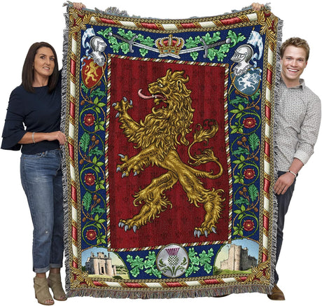 Two people holding a large decorative blanket with a lion emblem and intricate border.
