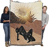 Two people holding a large blanket with a sun and silhouette design.