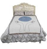 Tapestry blanket showing hands and above them, a blue orb of constellations, on a bed