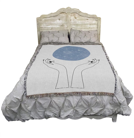 Tapestry blanket showing hands and above them, a blue orb of constellations, on a bed
