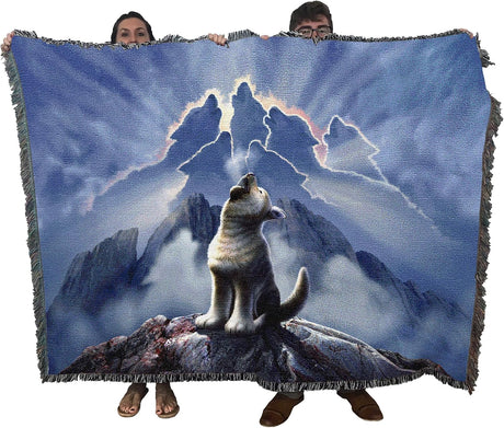 Tapestry blanket showing wolf cub howling, more wolves formed of clouds in the sky. Held up by two adults to show blanket's large size