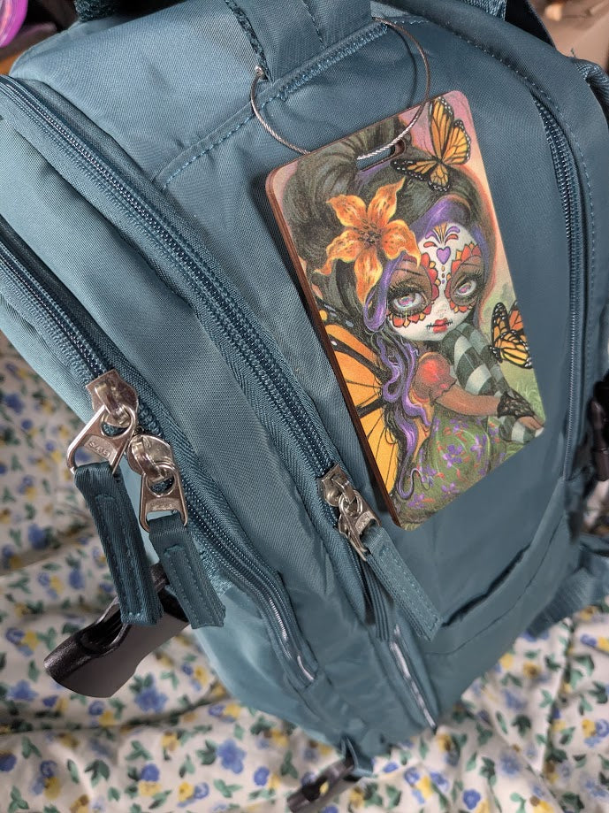 Blue suitcase with a decorative luggage tag featuring a fairy and butterfly design.