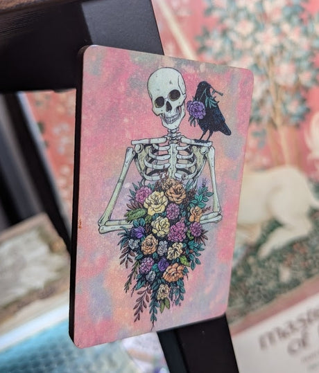 Magnet of skeleton holding flower bouquet with raven on shoulder, pink background