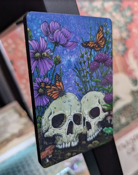 Magnet with two skulls, flowers, and butterflies on a blue background