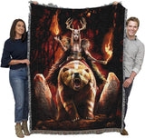Woven blanket with a fantasy design of a warrior woman on a bear with flames and stone carvings, held by two people to show large size