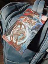 Luggage tag with fantasy design of a wizard holding an orb with a dragon inside, shown on a teal bag