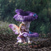 Blond pixie with pink and yellow wings sits under purple flowers with two blue birds