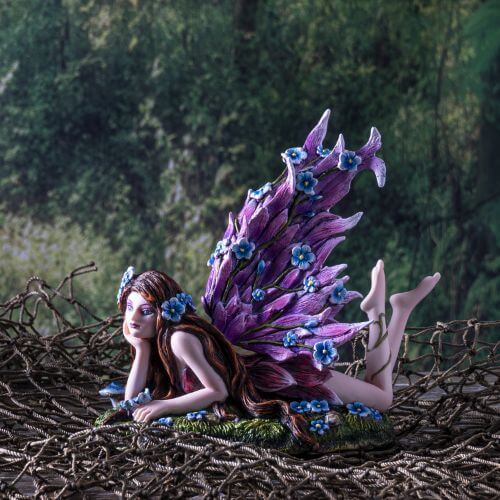 Fairy with pink wings  and long brown hair, covered in blue flowers laying in a meadow